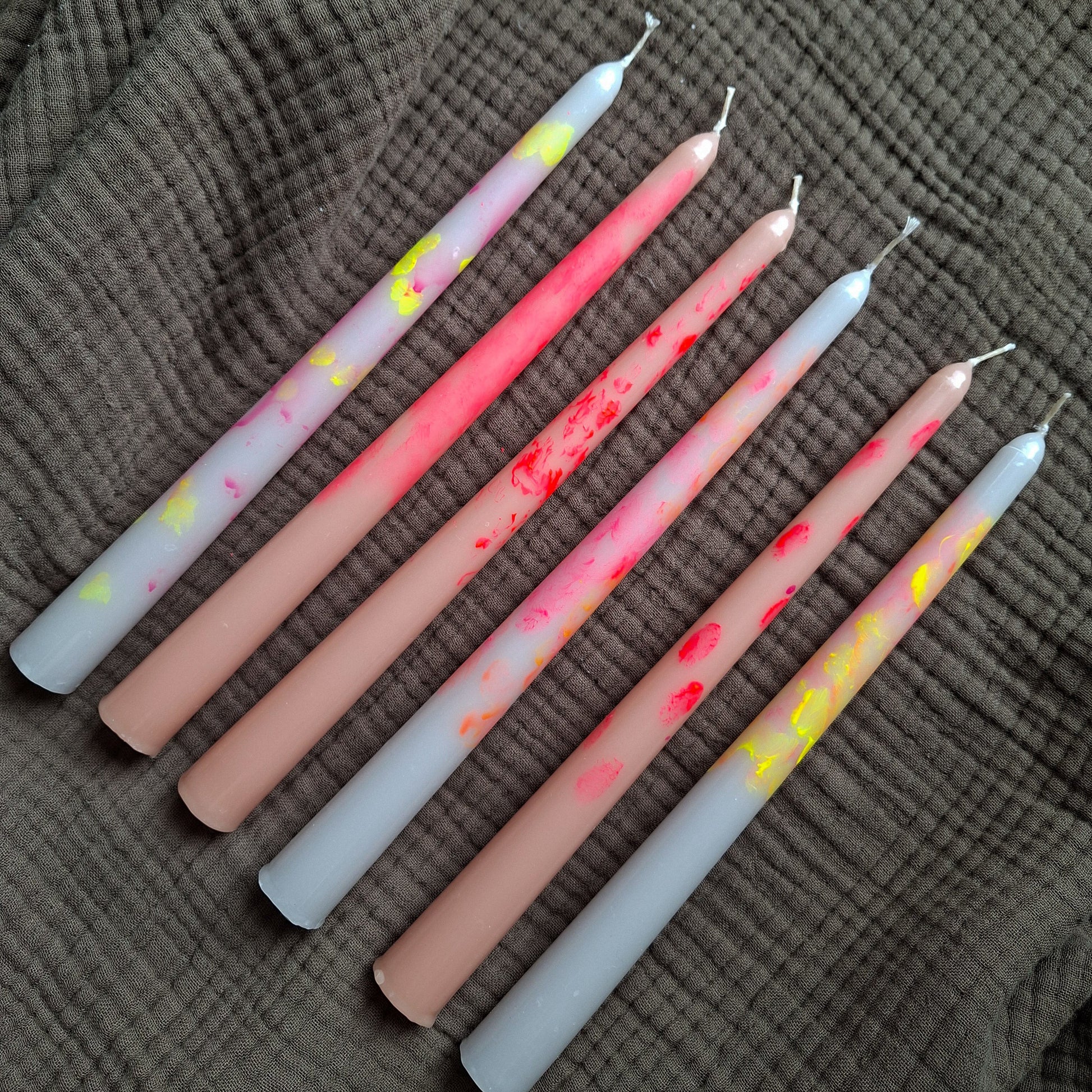 Handgemachte Dip-Dye Stabkerzen in Pastell- und Neonfarben auf braunem Stoff – moderne bunte Kerzen für Dekoration und Tischdeko