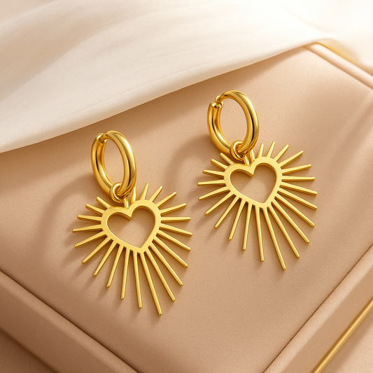 Goldene Herz-Sonnenstrahlen-Ohrringe aus Edelstahl – elegante Damen Ohrringe auf beigem Schmuck-Etui mit Stoffhintergrund
