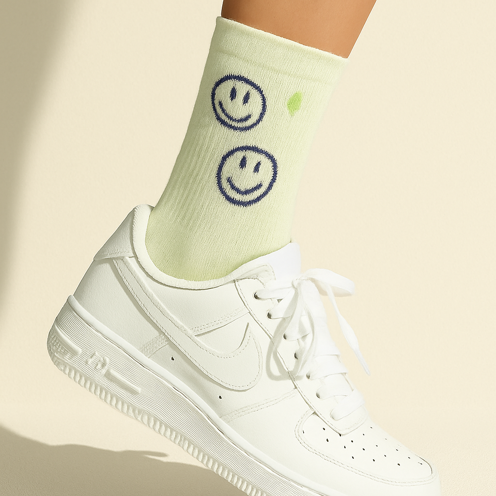 Pastellgrüne Crew-Socken mit dunkelblauer Smiley-Stickerei und grünem Blitzsymbol, getragen mit weißen Sneakers auf hellem Hintergrund.