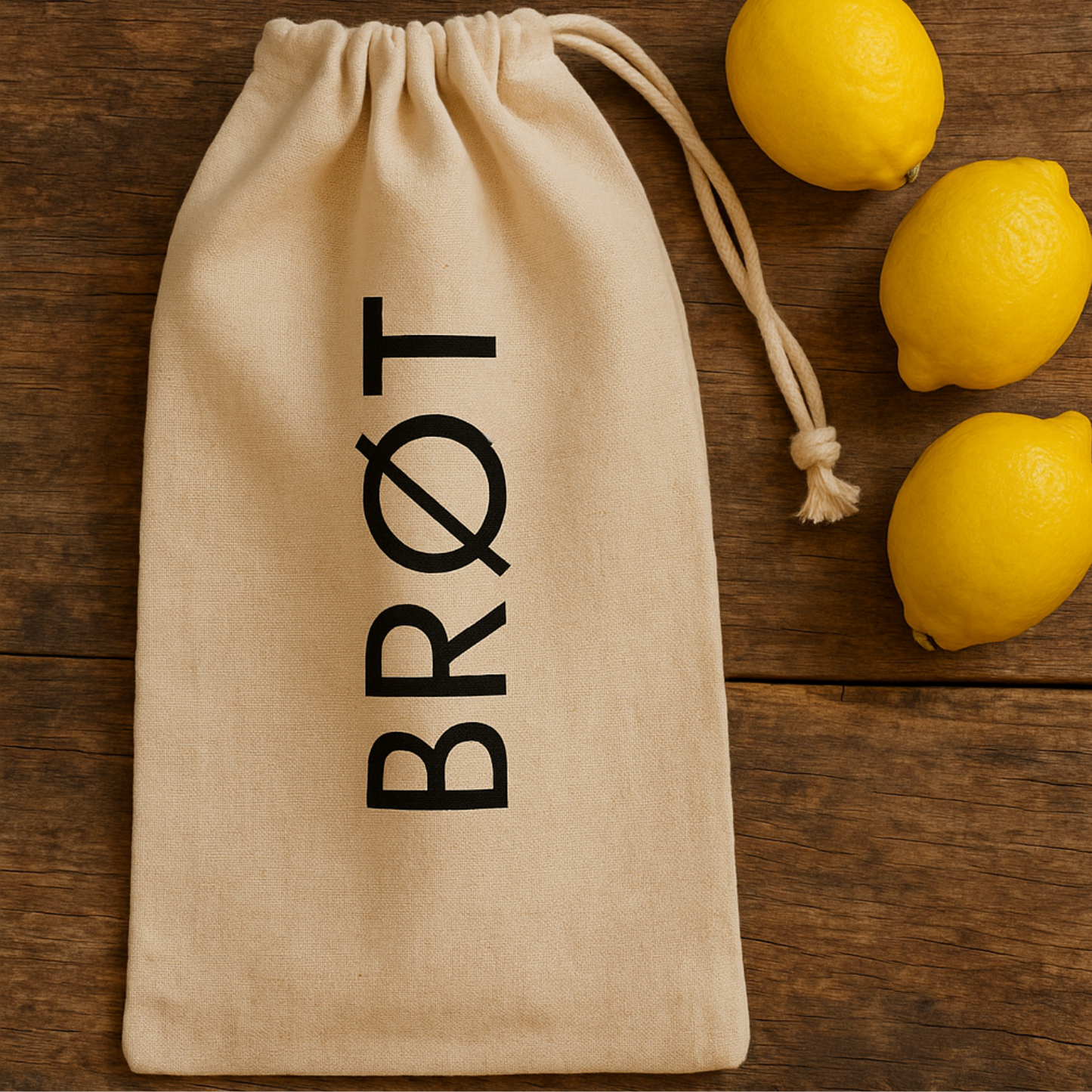 Leinen Brotbeutel mit schwarzem BRØT-Aufdruck auf hellem Holztisch, daneben drei Zitronen – skandinavisch, minimalistisch, natürlich.